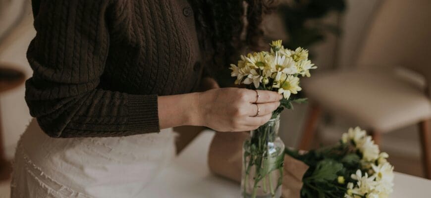 A woman places a small bouquet of flowers in a small glass vase